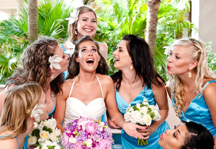 Ecstatic bride surrounded by her bridesmaids dressed in a teal blue. The bride holds pink flowers and the bridesmaids hold white flowers