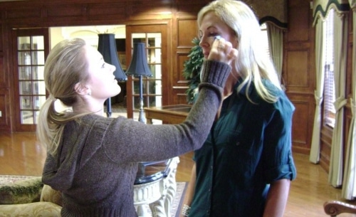 Applying makeup to the face of a tall blonde woman