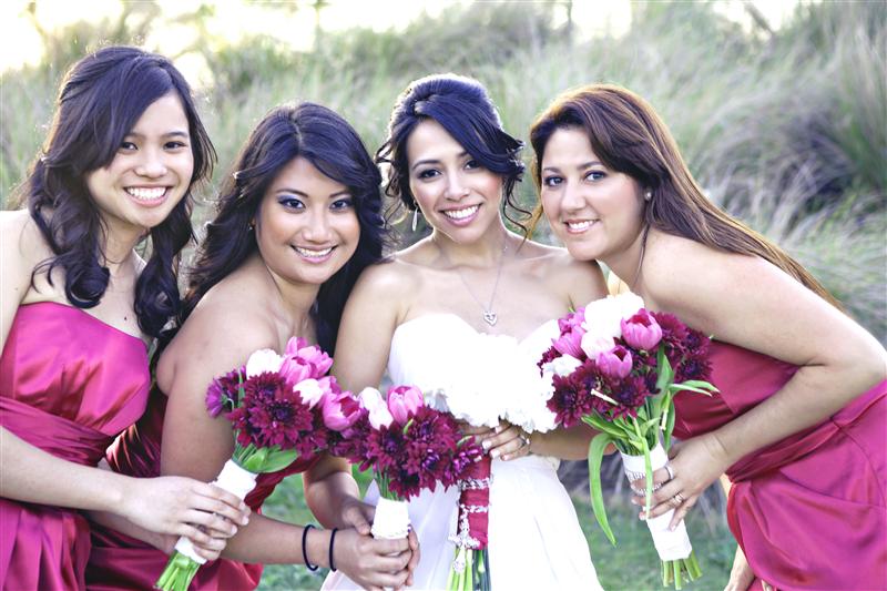 Bride smiling with her bridesmaids. They are wearing marroon dresses and hold marroon flowers