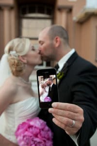 Bride and groom take a selfie while kissing