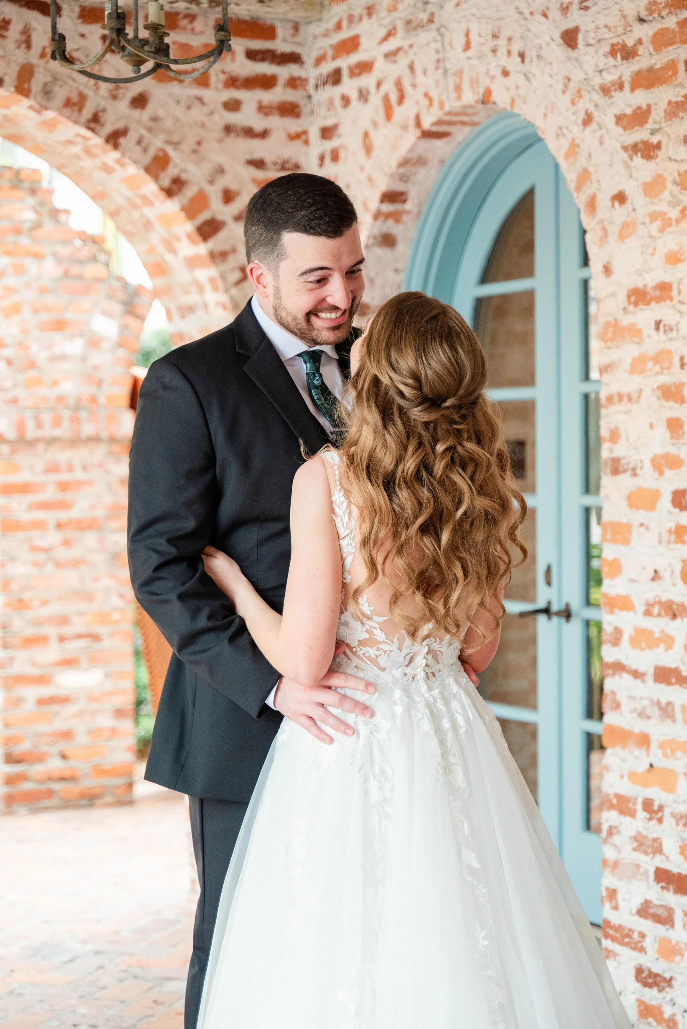 bridal hair makeup romantic waves m3 beauty orlando wedding - Wedding Makeup and Hair Gallery Bride with long romantic curled waves hairstyle and natural makeup by M3 Beauty embracing groom at Orlando wedding venue with exposed brick walls and turquoise doors